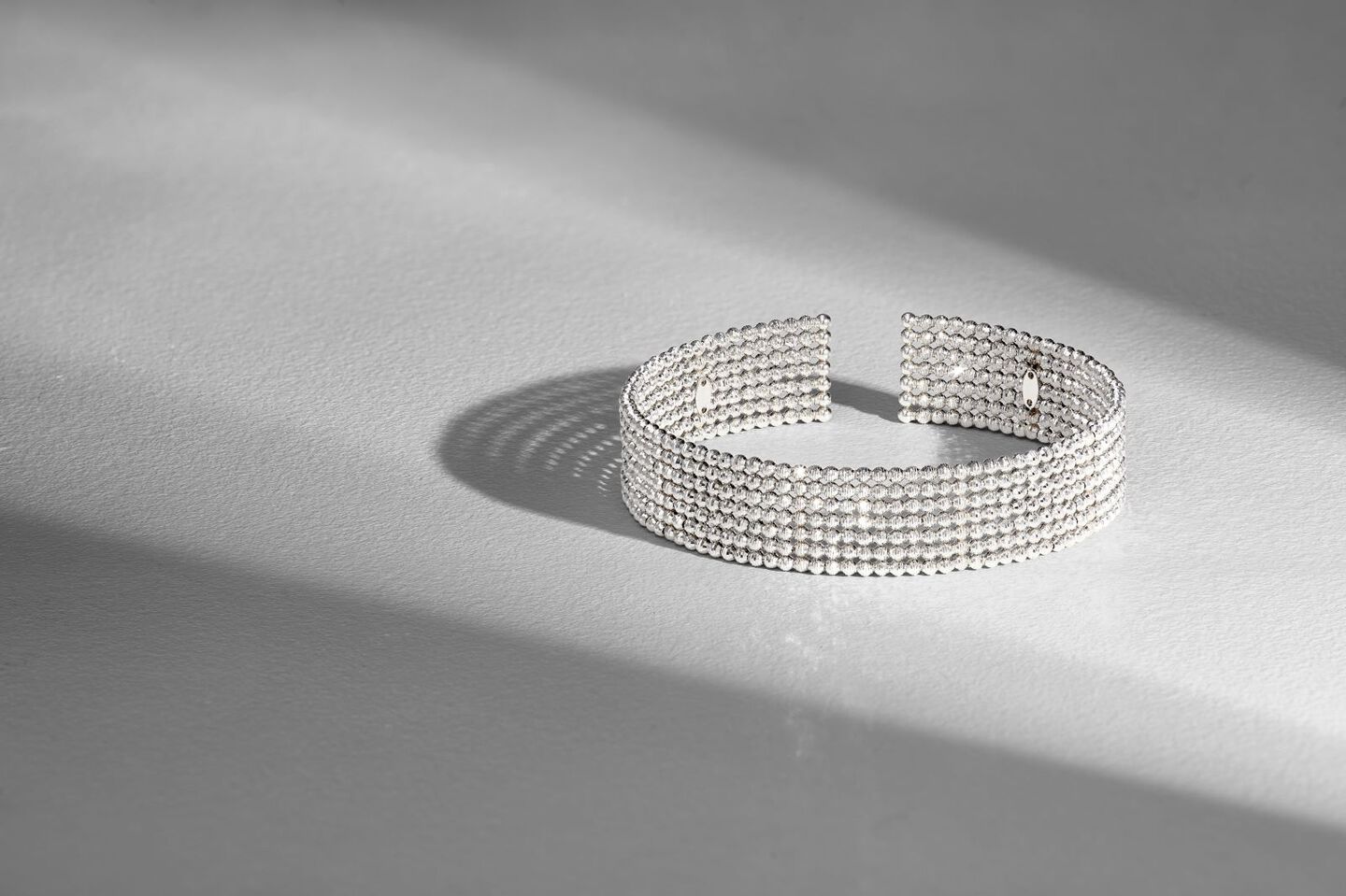 A platinum bracelet on a gray background between two shadows